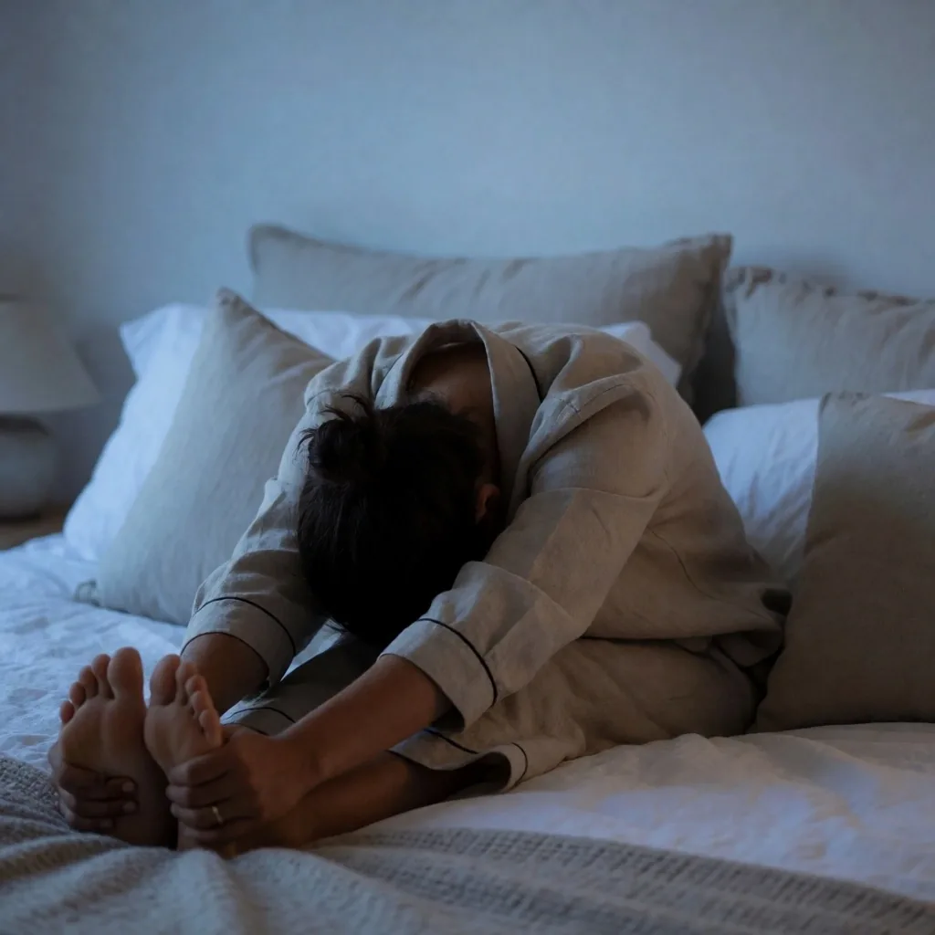 Person in einer ruhigen Yoga-Position am Bett bei blauem Dämmerungslicht